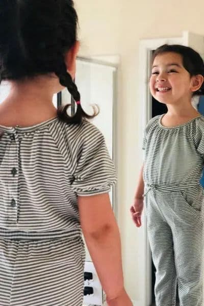 Smiling girl in striped outfit looking at her reflection in the mirror.
